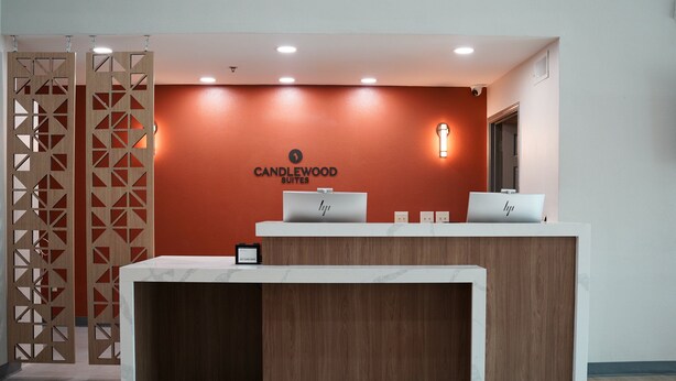 A reception desk with a wooden finish and a red accent wall. There are two laptops on the desk, and a sign above reads "CANDLEWOOD SUITES." - Candlewood Suites Houston Space Center – Webster (Webster)