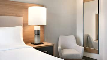 Une chambre d’hôtel avec un lit, une table de chevet avec une lampe, une chaise et un grand miroir au mur.