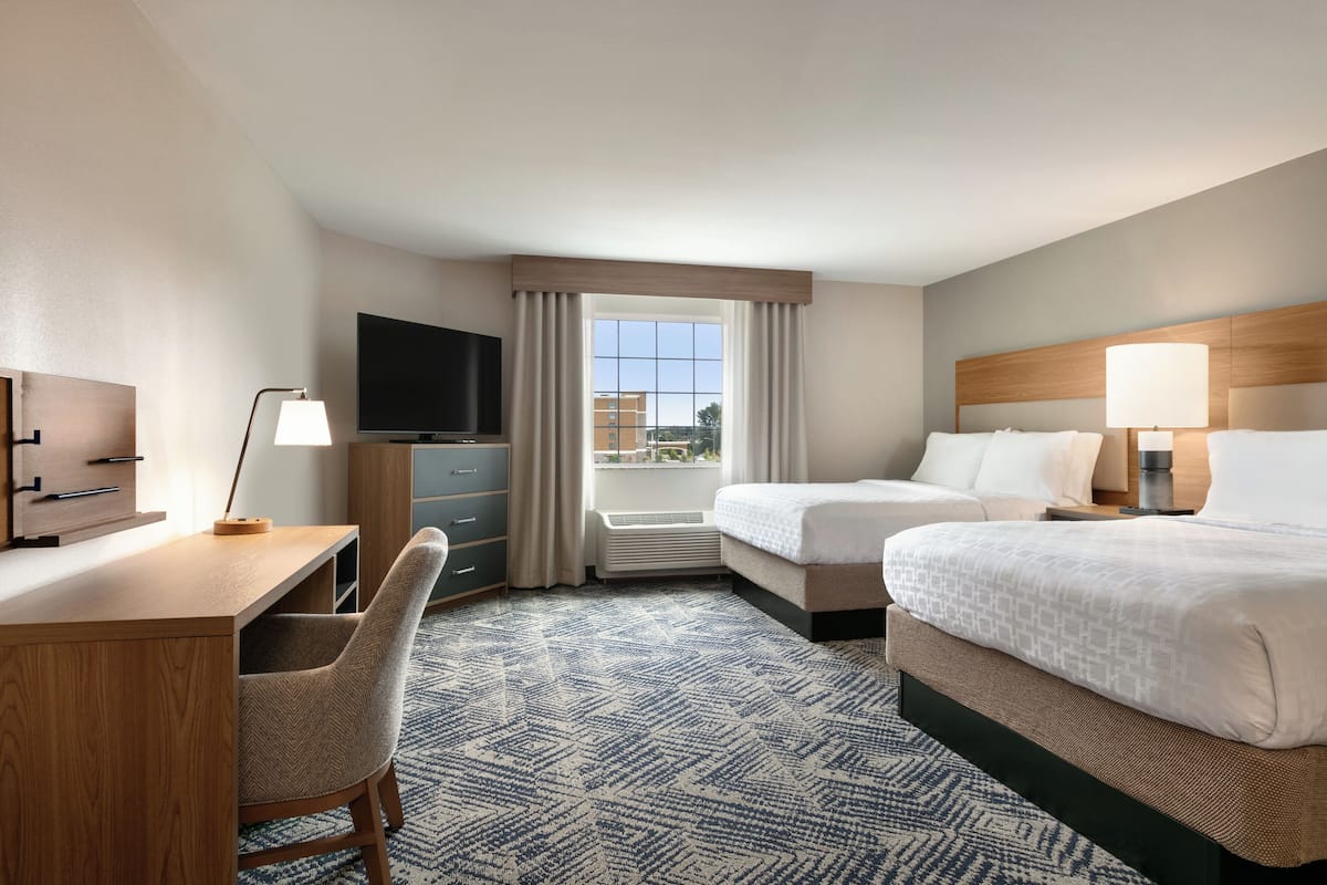 A hotel room with a desk, two beds, a TV, and a window with curtains.