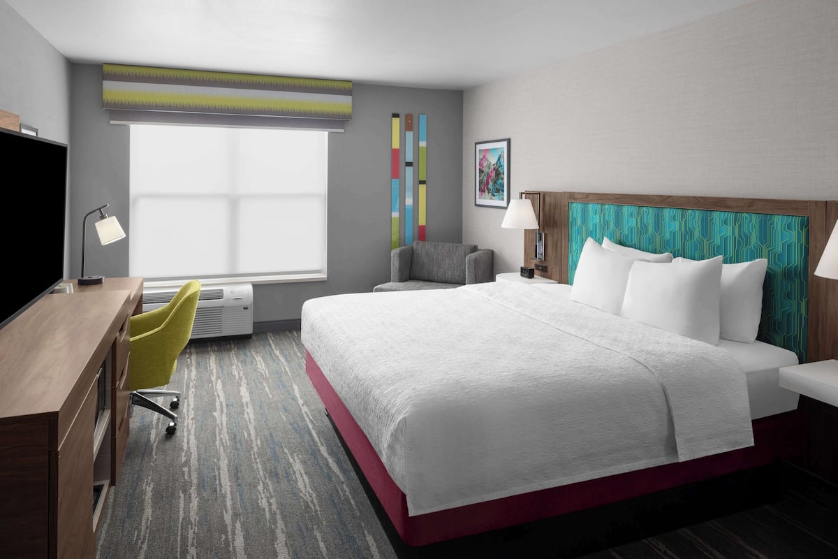 Habitación de hotel con una cama grande, un escritorio, una silla y una ventana con persianas.