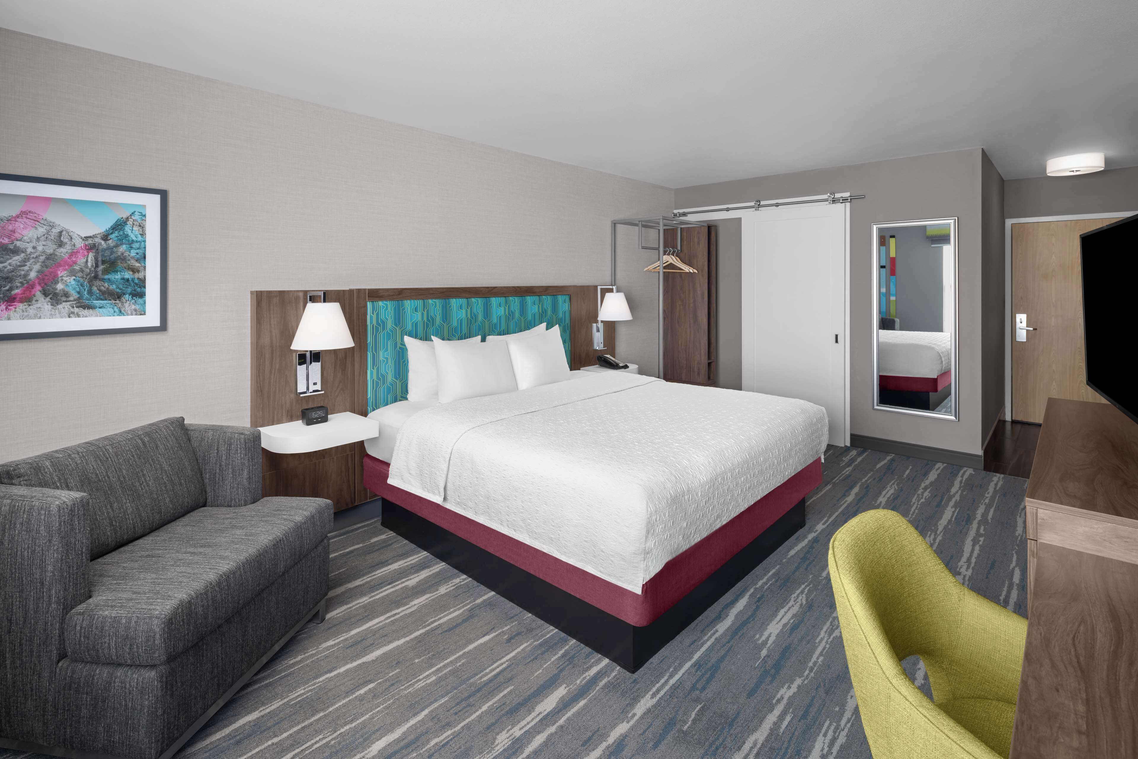 A hotel room with a bed, a sofa, a chair, a desk, and a painting on the wall.