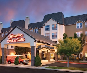 A Hampton Inn & Suites hotel with a modern design, featuring a prominent neon sign, a well-lit entrance, and a red van parked in front.