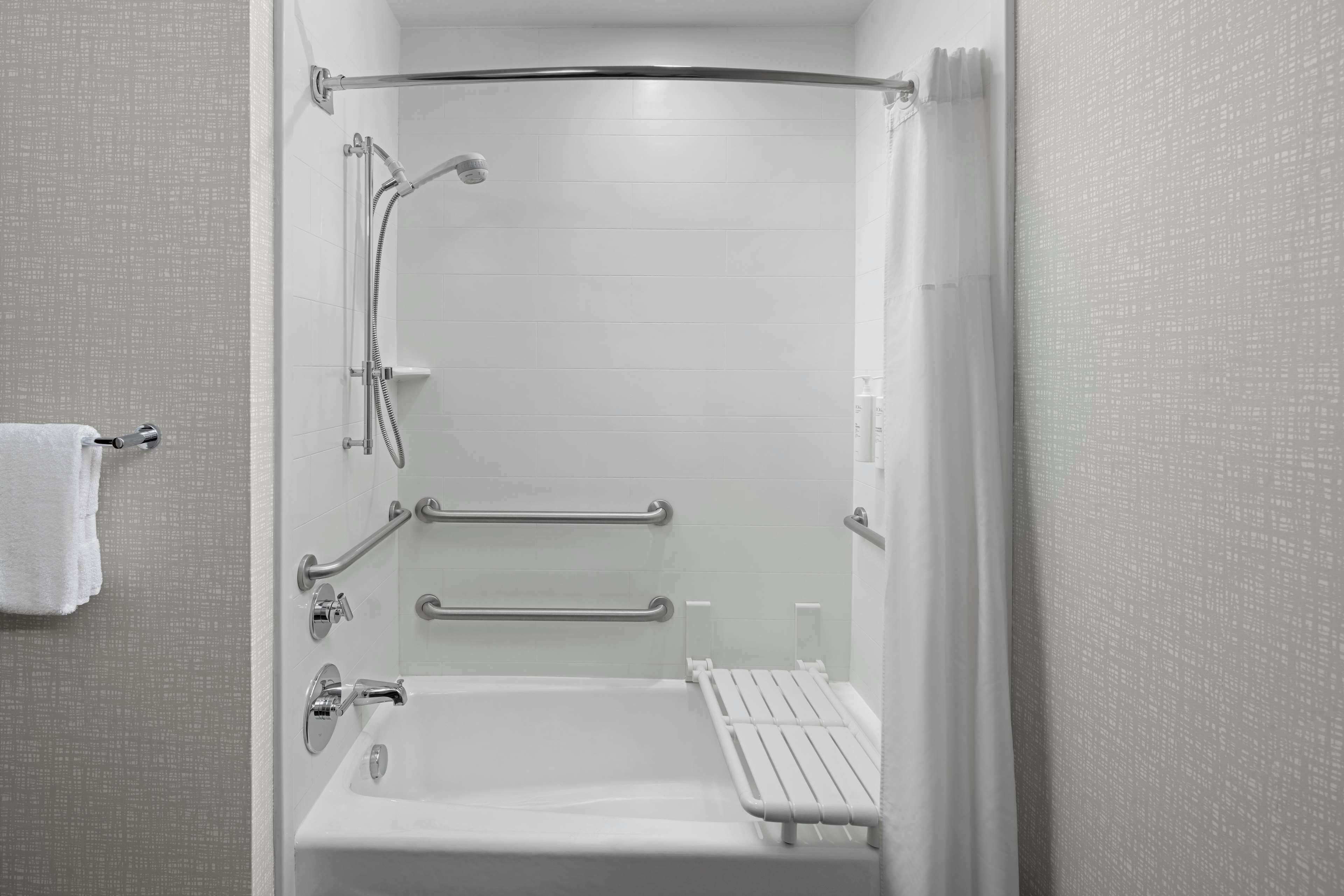 Un baño moderno con ducha a ras de suelo, barras de apoyo y un asiento.