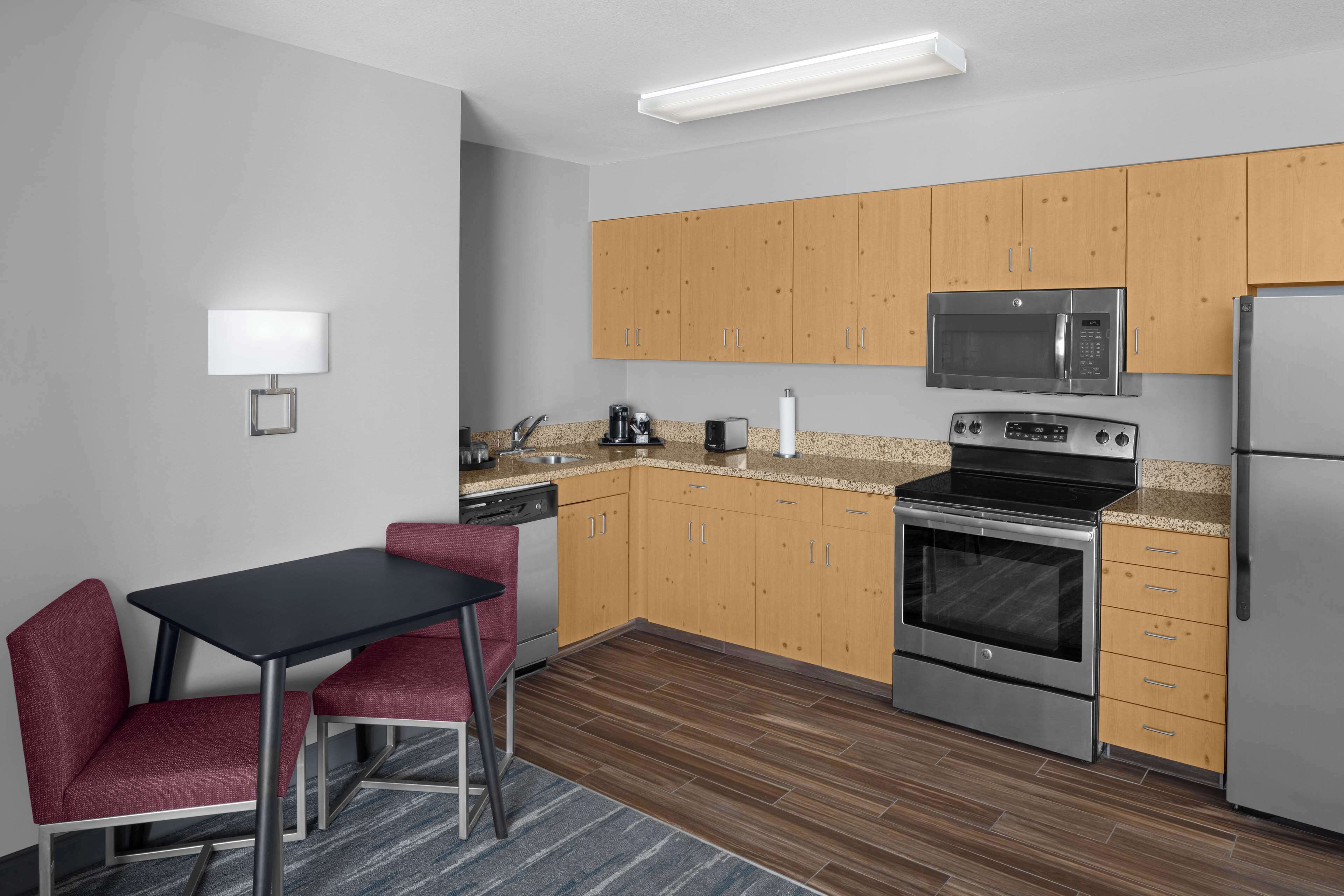 A compact kitchen with wooden cabinets, a microwave, a stove, and a refrigerator. There is a small dining table with two chairs.