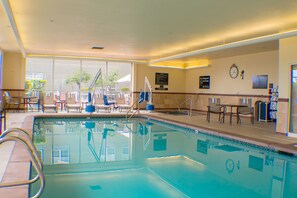 A swimming pool with a lifeguard chair, lounge chairs, and a clock on the wall.