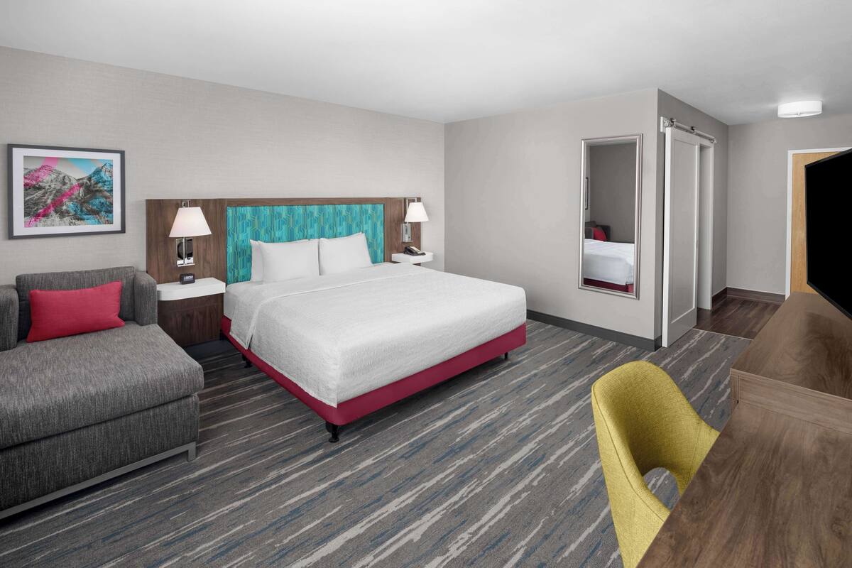 Una habitación de hotel con una cama, un sofá, una silla, un escritorio y un espejo.