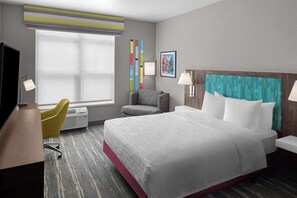 A hotel room with a large bed, a desk with a chair, a window with blinds, and a wall with a colorful artwork.