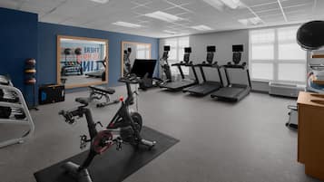 Une salle de sport équipée de machines de cardio, d’un miroir et d’une affiche motivante.