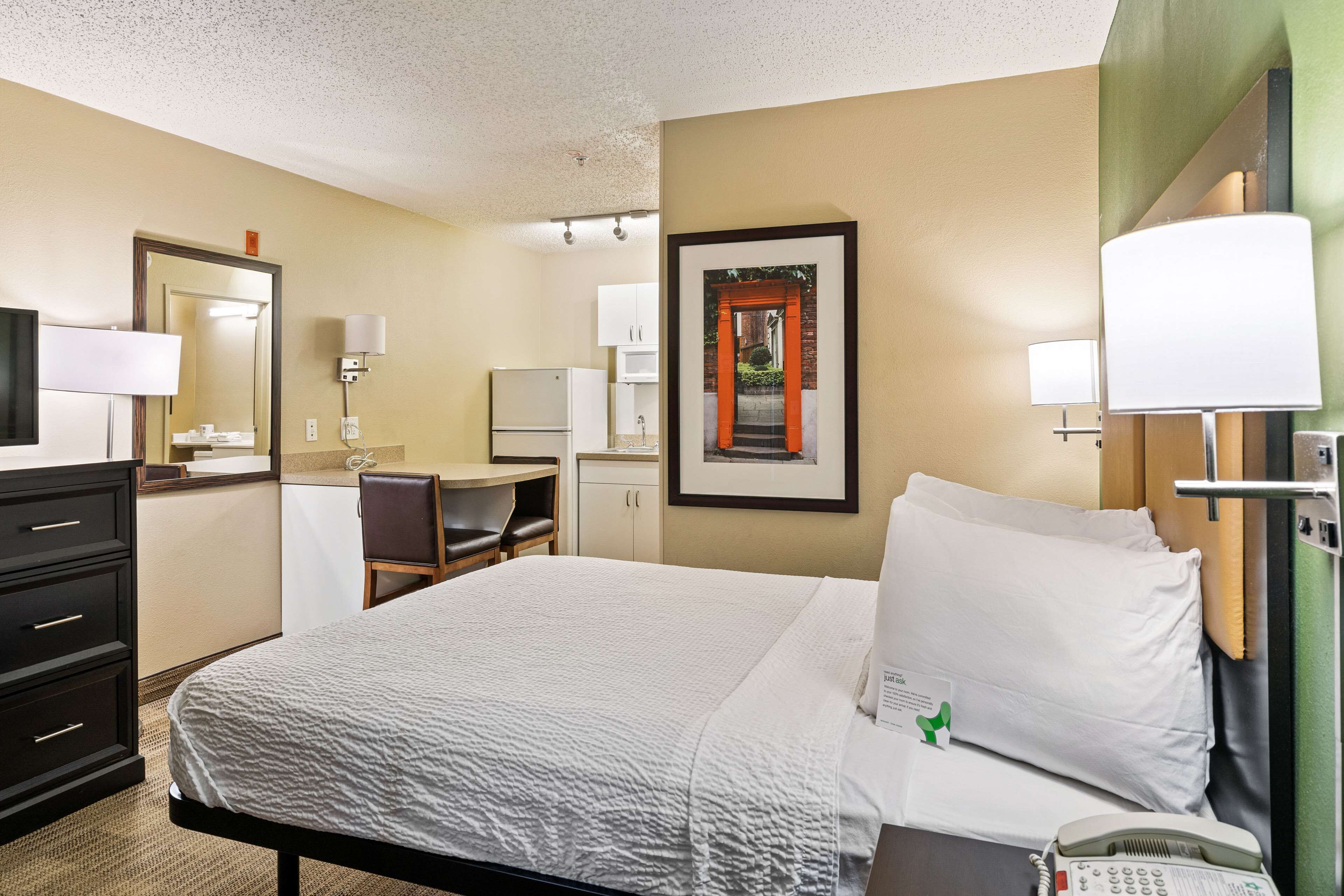 A hotel room with a bed, a desk, a chair, a telephone, and a framed picture on the wall.