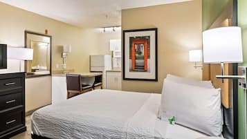 Una habitación de hotel con cama, escritorio, silla, teléfono y un cuadro en la pared.