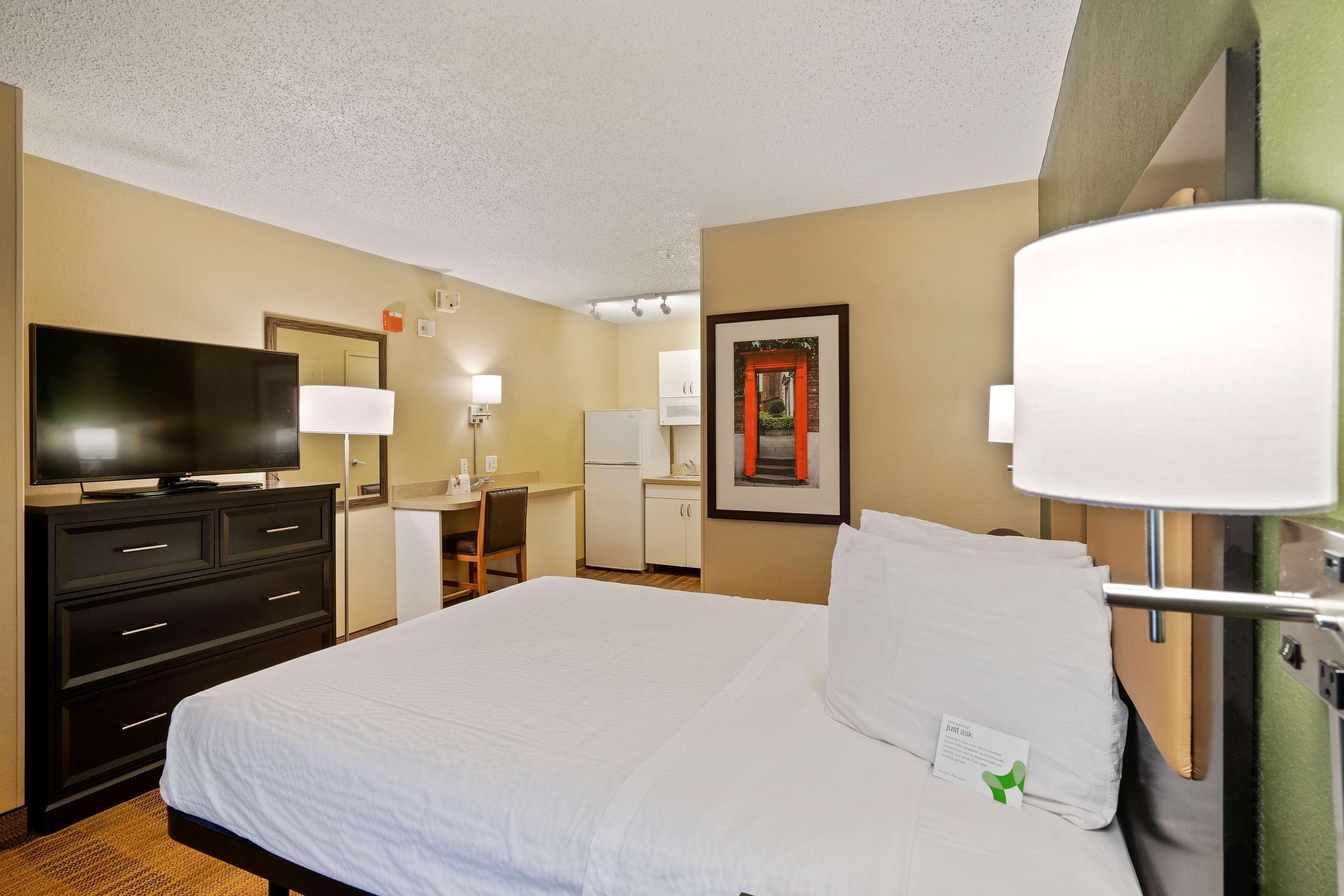 Quarto de hotel com uma cama, uma escrivaninha, uma televisão e um espelho.