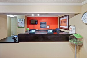 Un mostrador de recepción de hotel con un quiosco digital, un reloj y un cartel de bienvenida.