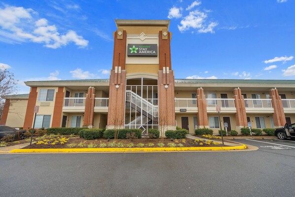 A Stay America hotel with a brick facade, a central staircase, and a parking lot.
