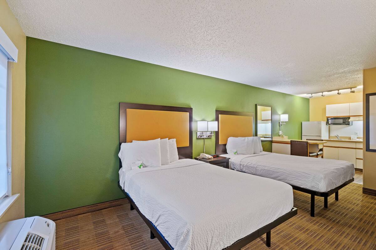 A hotel room with two beds, a desk, a microwave, and a small kitchenette.