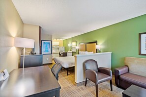 A hotel room with a bed, desk, chairs, and a reception desk.
