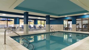 An indoor swimming pool with clear blue water, surrounded by lounge chairs and umbrellas, and a view of outdoor greenery through large windows. - Hampton Inn Roanoke/Hollins - I-81 (Roanoke)