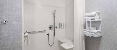 A modern bathroom with a walk-in shower, a toilet with a grab bar, and a shelf with neatly folded towels.