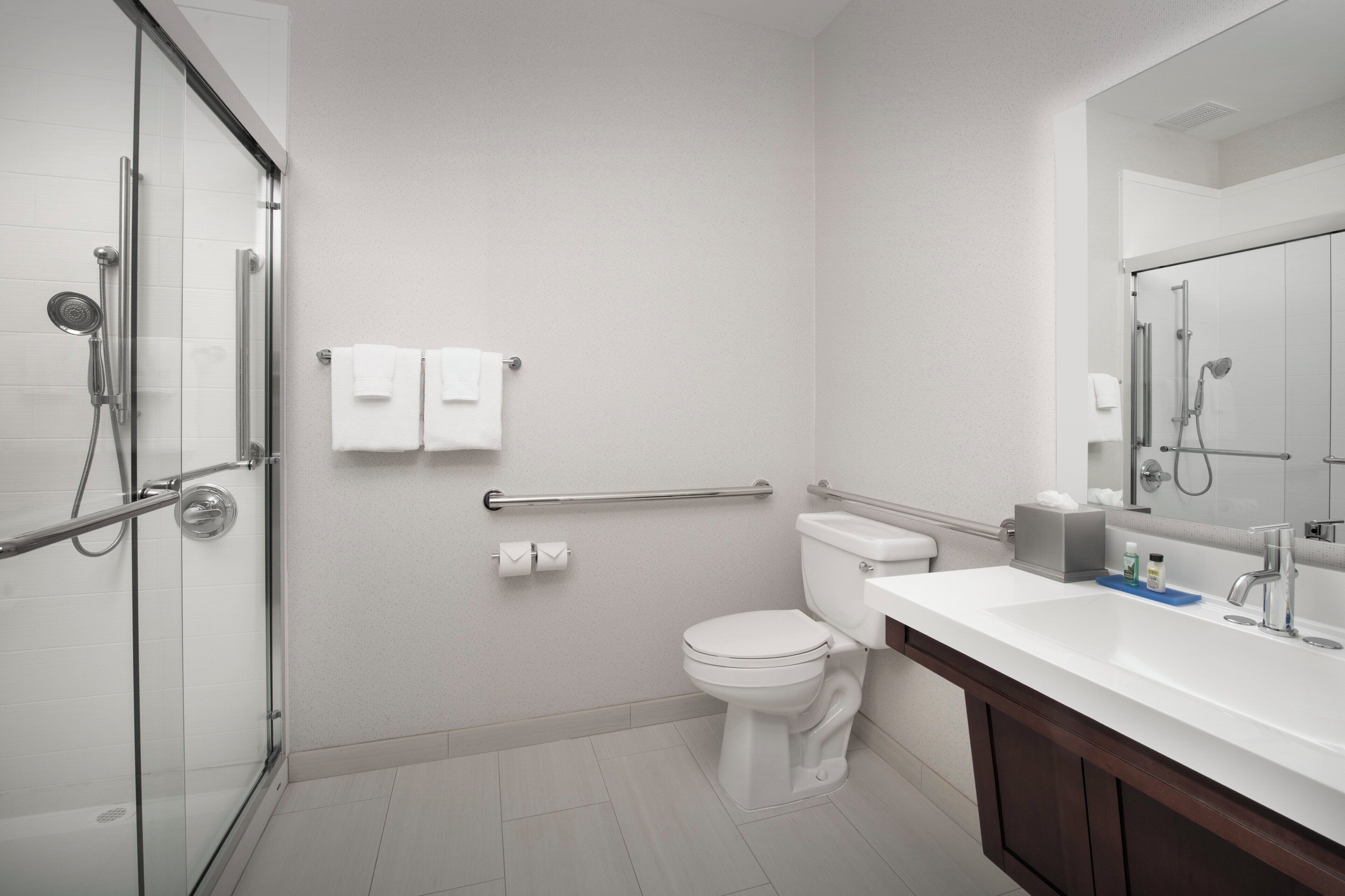 Une salle de bain moderne avec une douche à parois de verre, des toilettes blanches, un lavabo avec un miroir et un porte-serviettes.