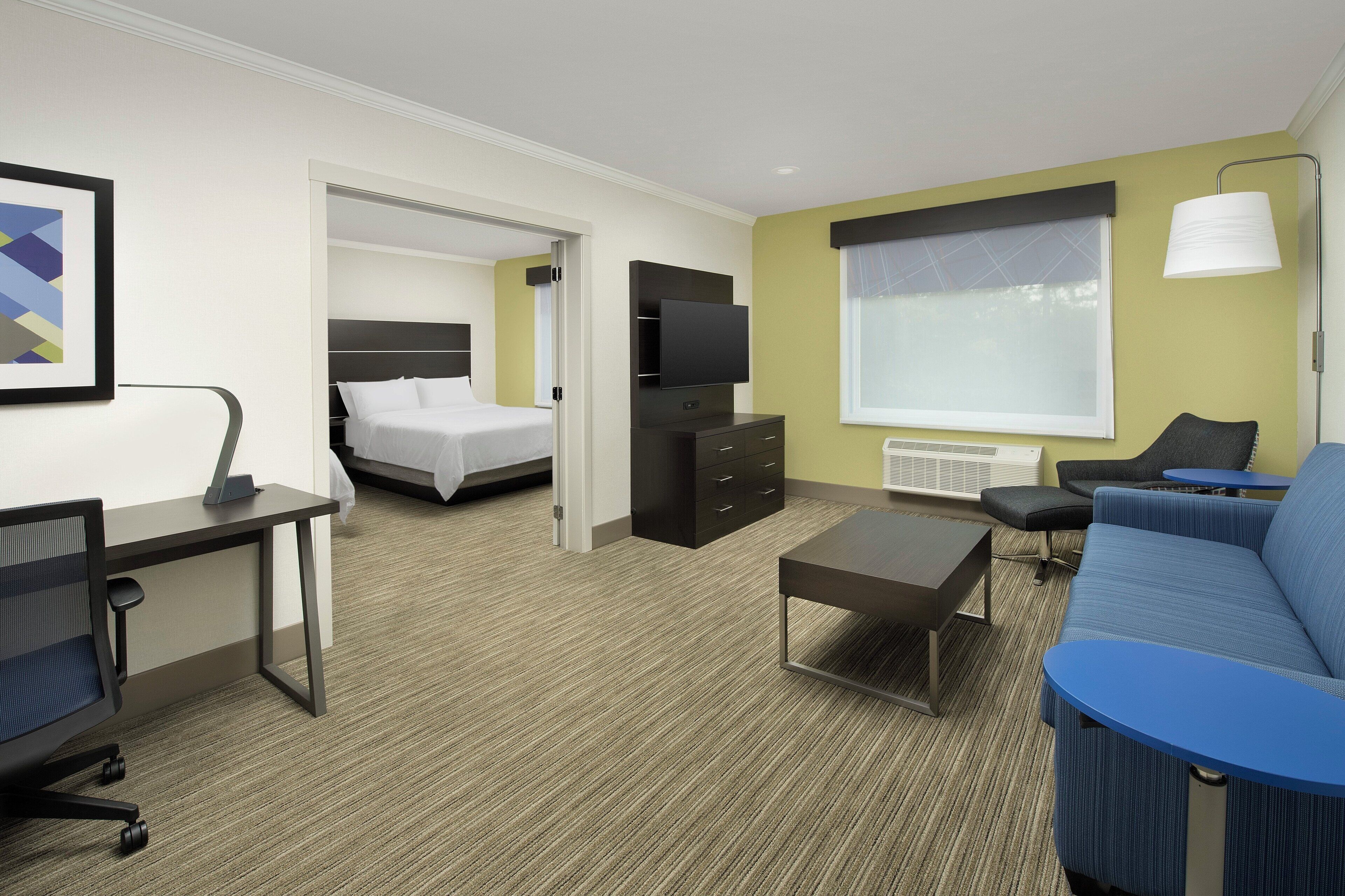 A hotel room with a bed, a desk with a chair, a sofa, a TV, and a window with a view.