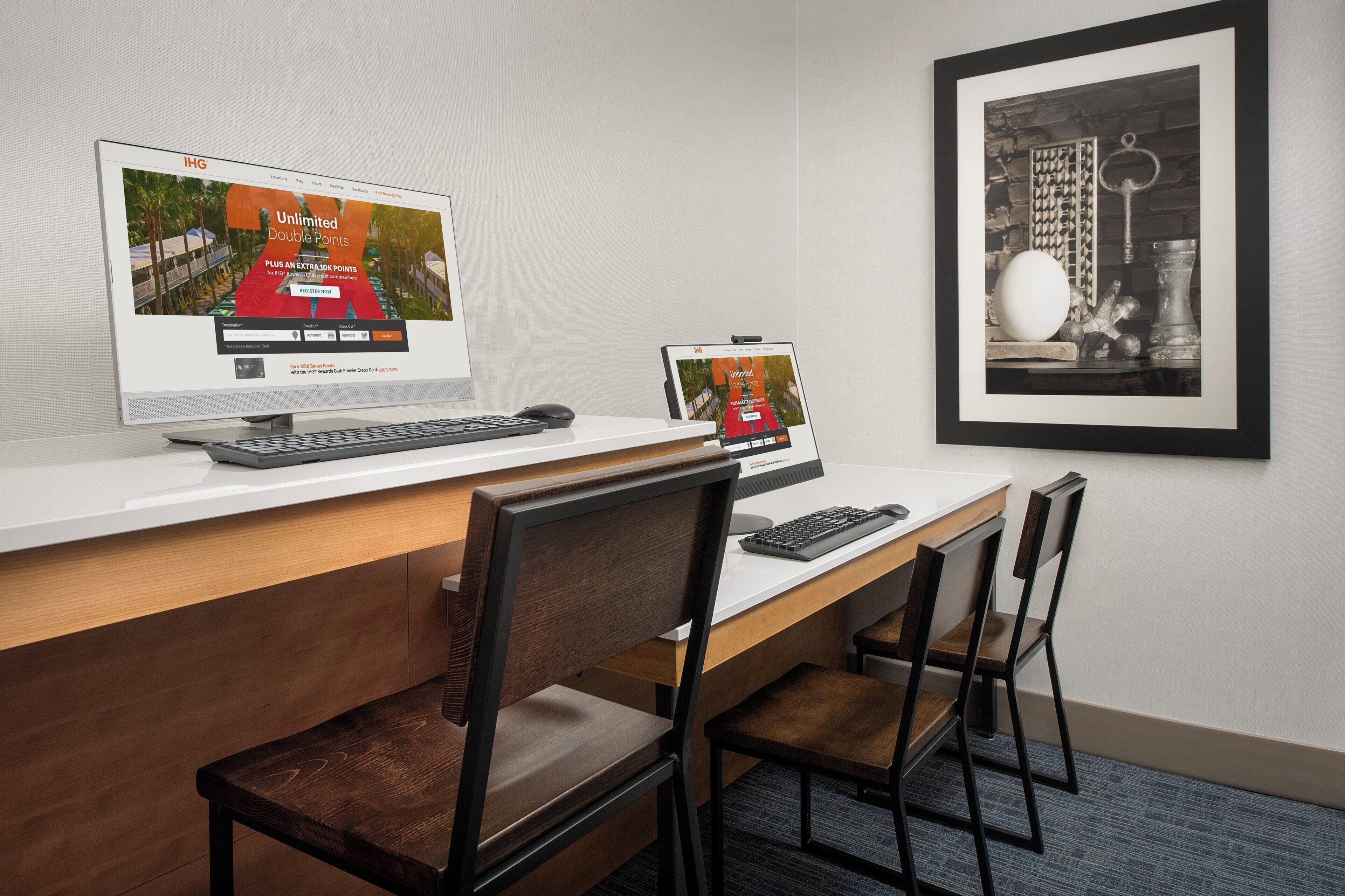 A hotel desk with two monitors displaying a rewards program, a keyboard, a mouse, and two chairs.