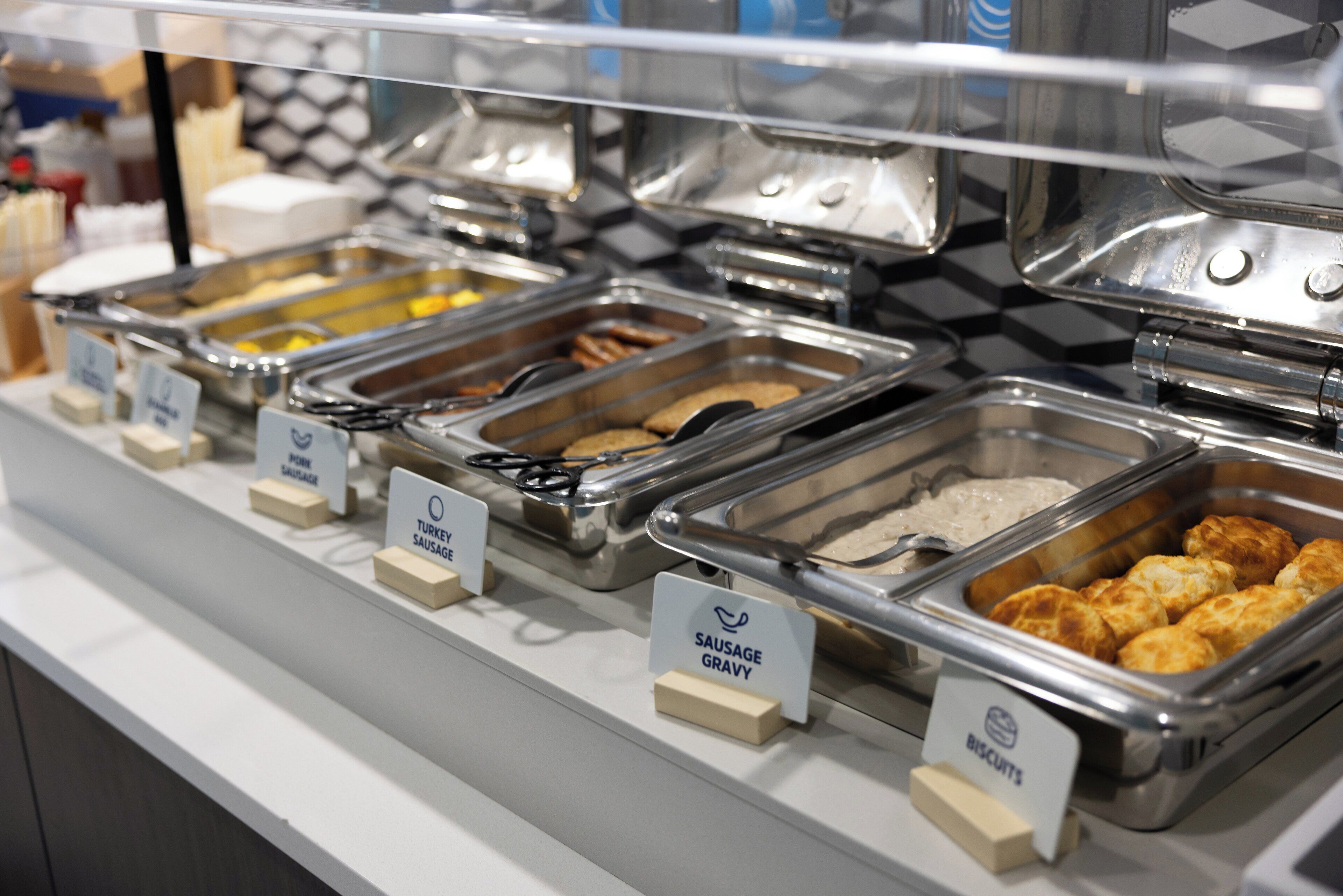 A buffet with labeled trays of food including turkey, sausage, gravy, and biscuits.