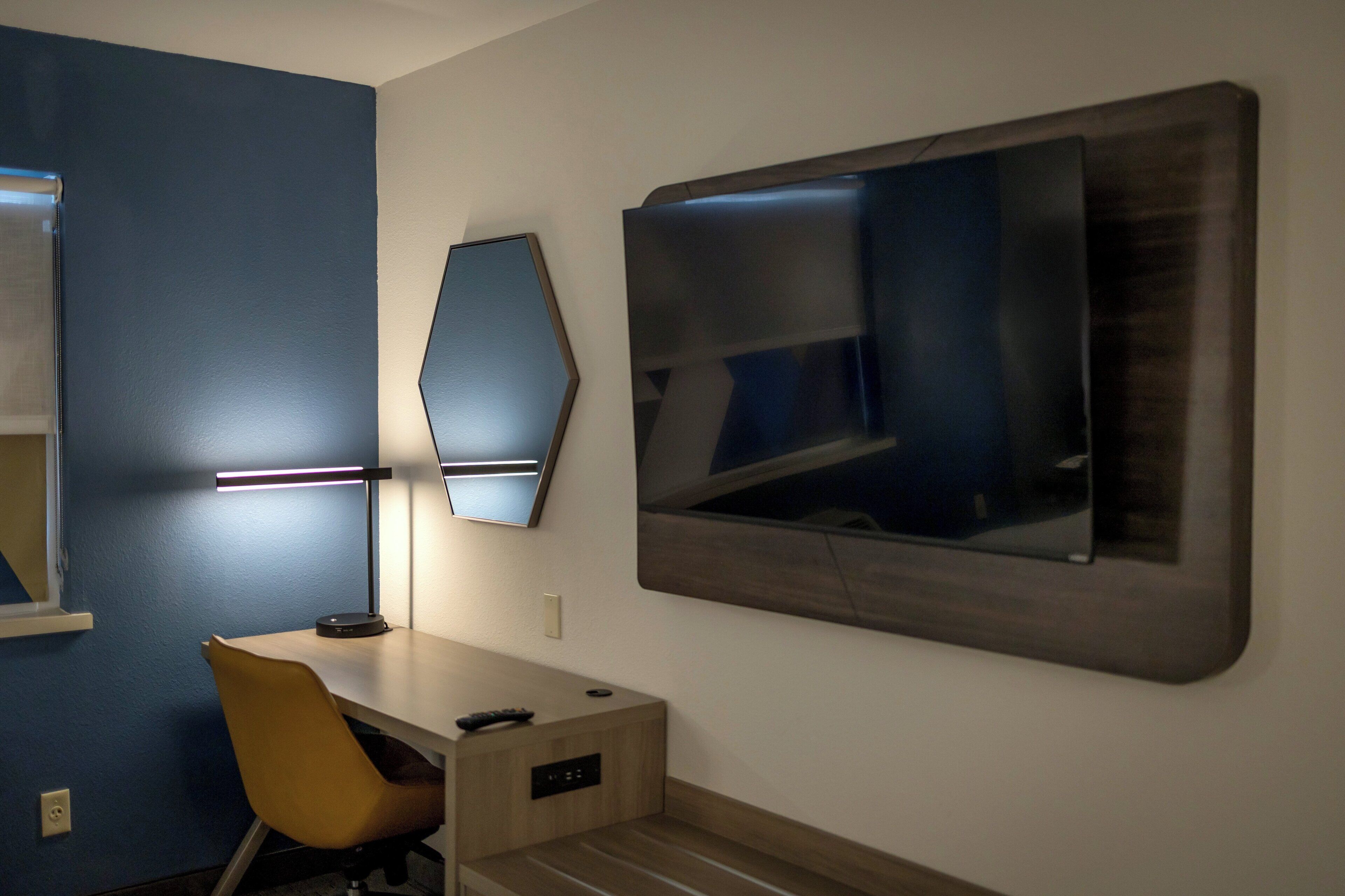 A modern room with a desk, chair, and a large mirror on the wall.