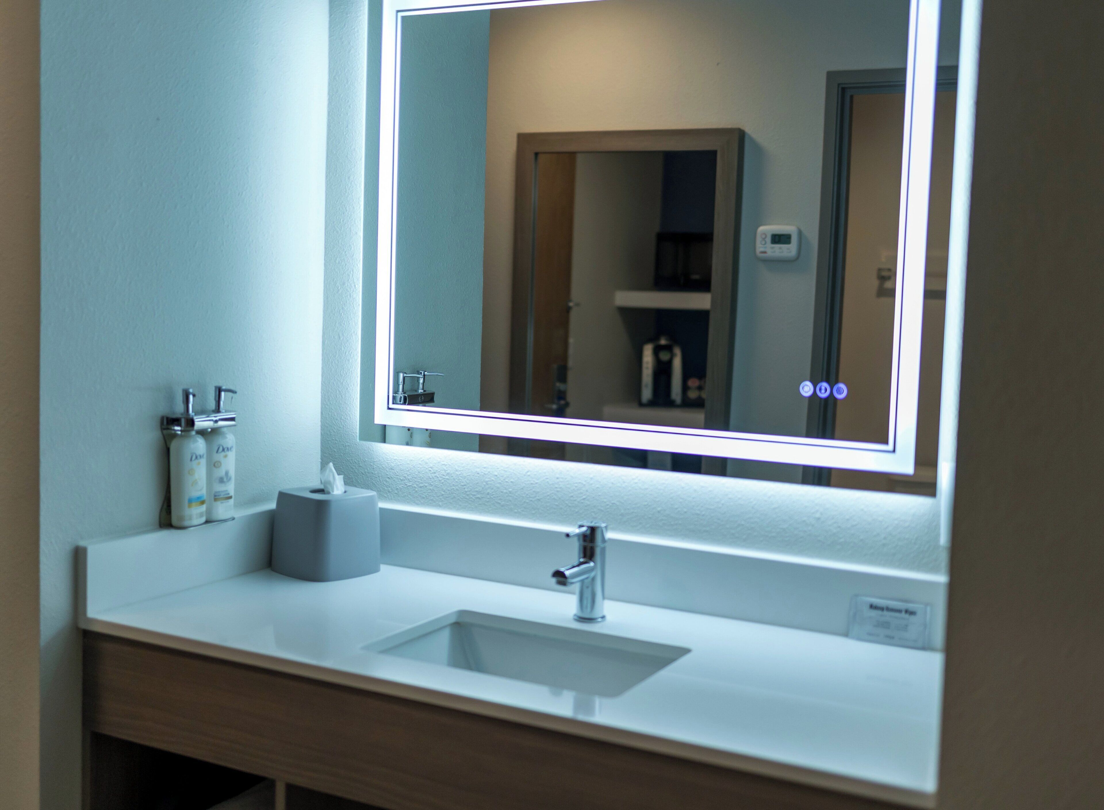 A bathroom with a white sink, a mirror with a lighted frame, and toiletries on the counter.