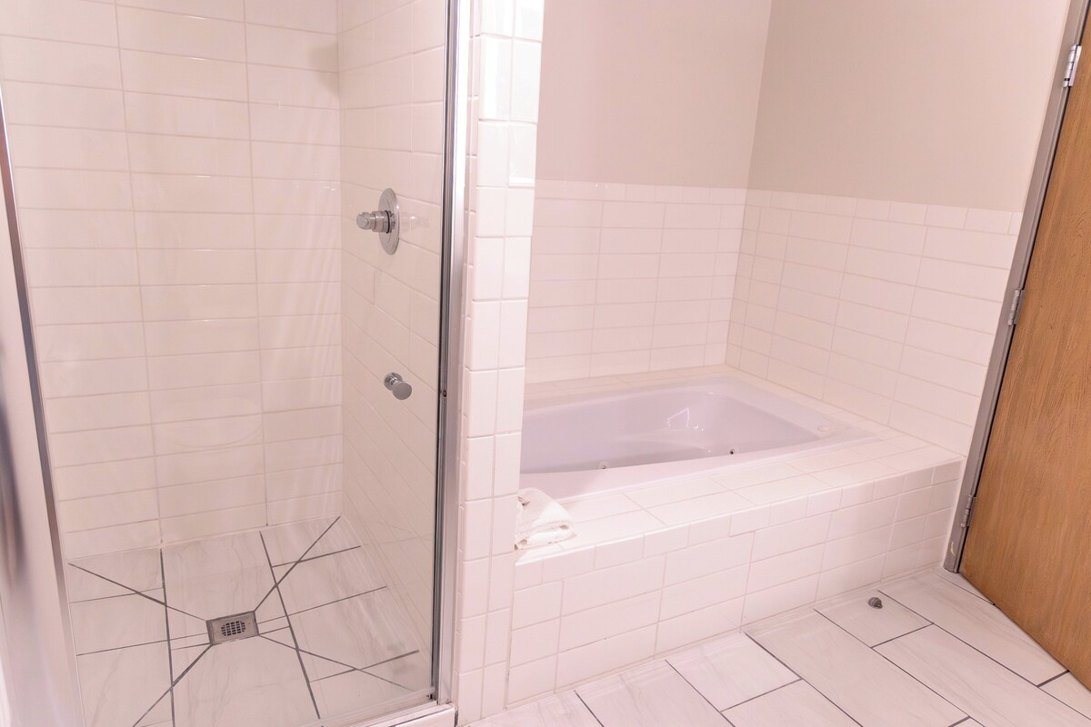 Une salle de bain avec une douche à parois de verre, une baignoire et des murs recouverts de carreaux blancs.