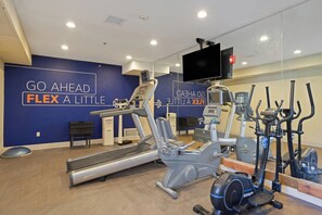 Une salle de sport équipée de machines de cardio, d’un tapis de course et d’un mur orné de citations motivantes.