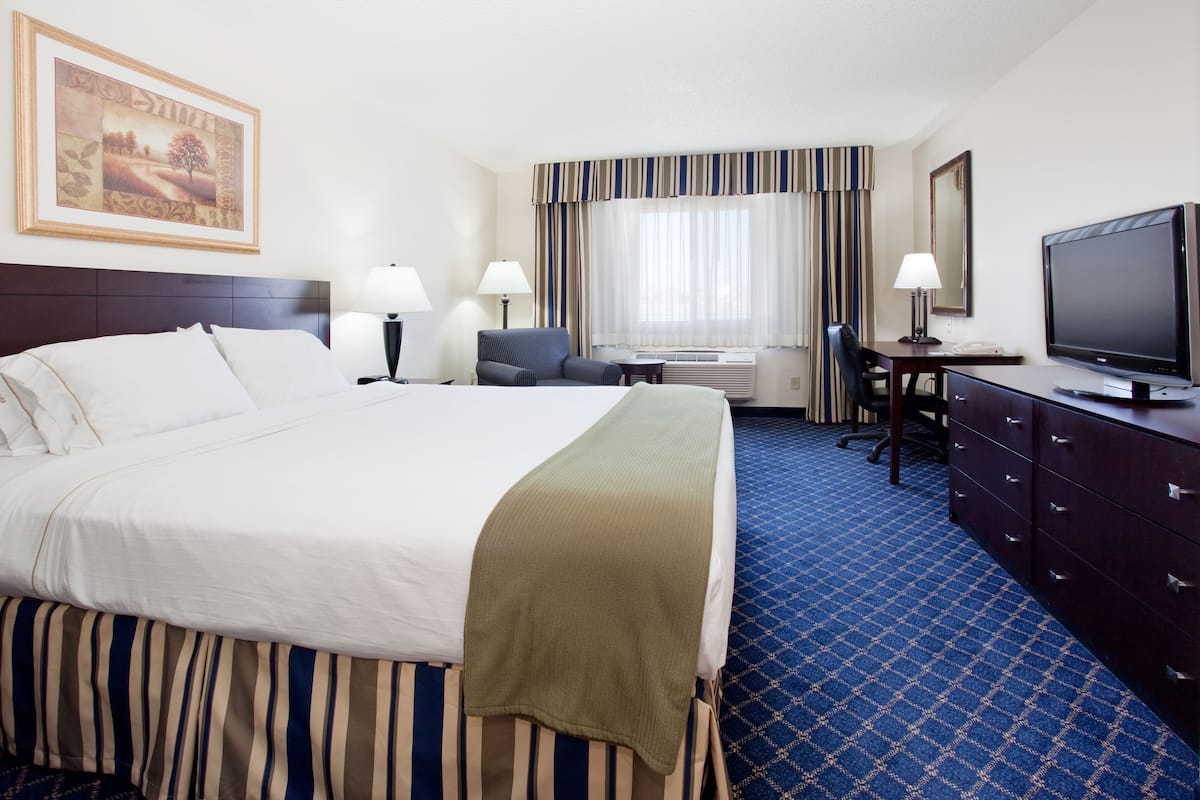 Una habitación de hotel con una cama grande, un escritorio con silla, un televisor y una ventana con cortinas.