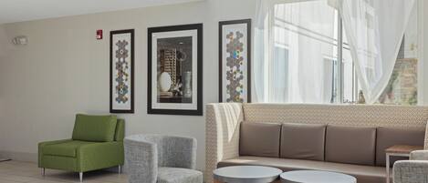 A modern living room with a green armchair, grey armchairs, a beige sofa, and two round tables.