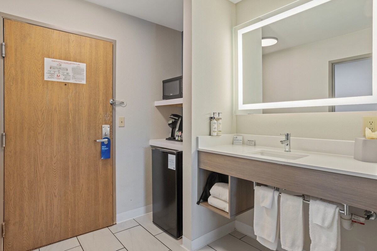Une salle de bain d’hôtel avec une porte en bois, un réfrigérateur, un four à micro-ondes, un lavabo et un miroir.