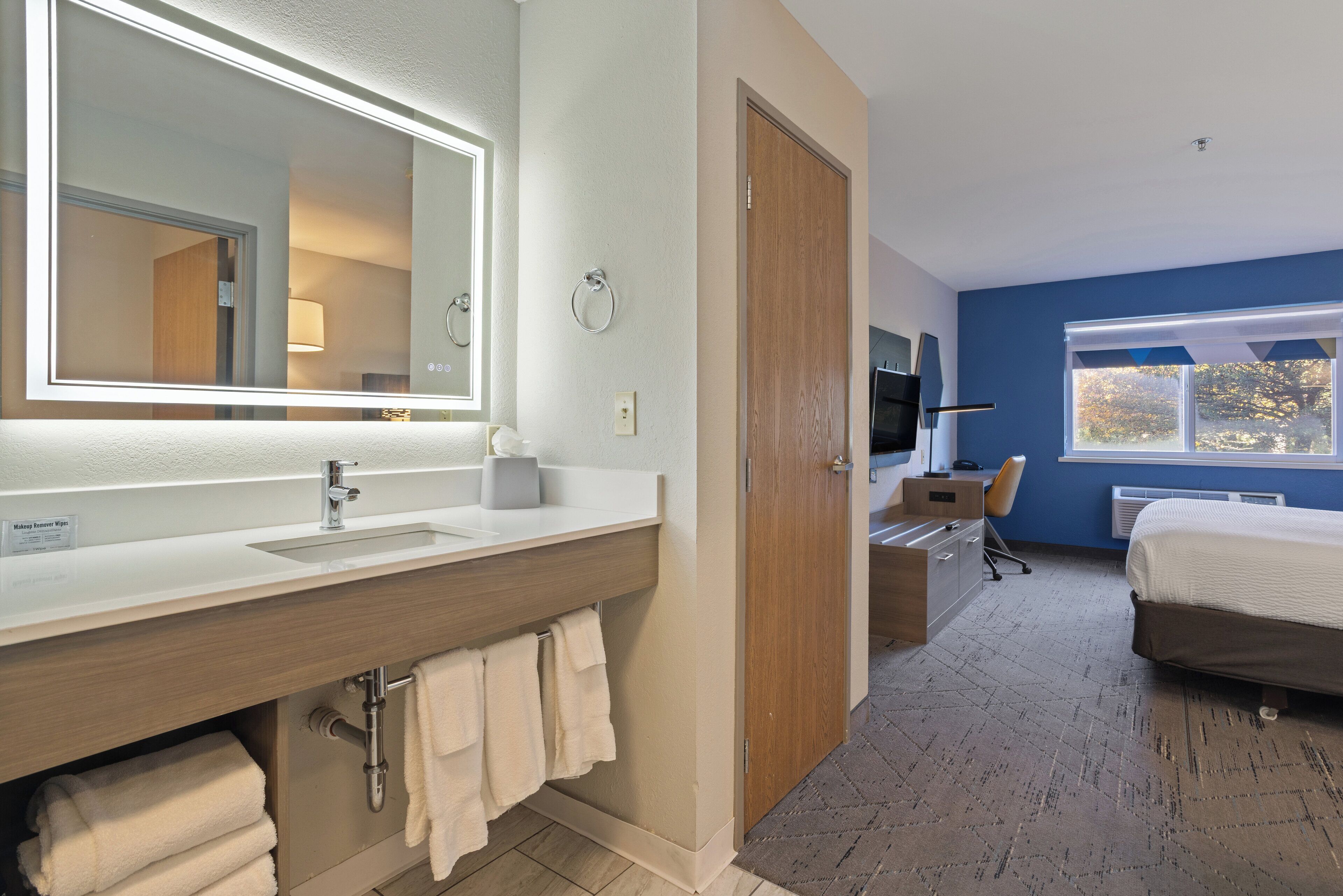 Una habitación de hotel con baño, cama, escritorio y televisor.