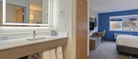 Una habitación de hotel con baño, cama, escritorio y televisor.