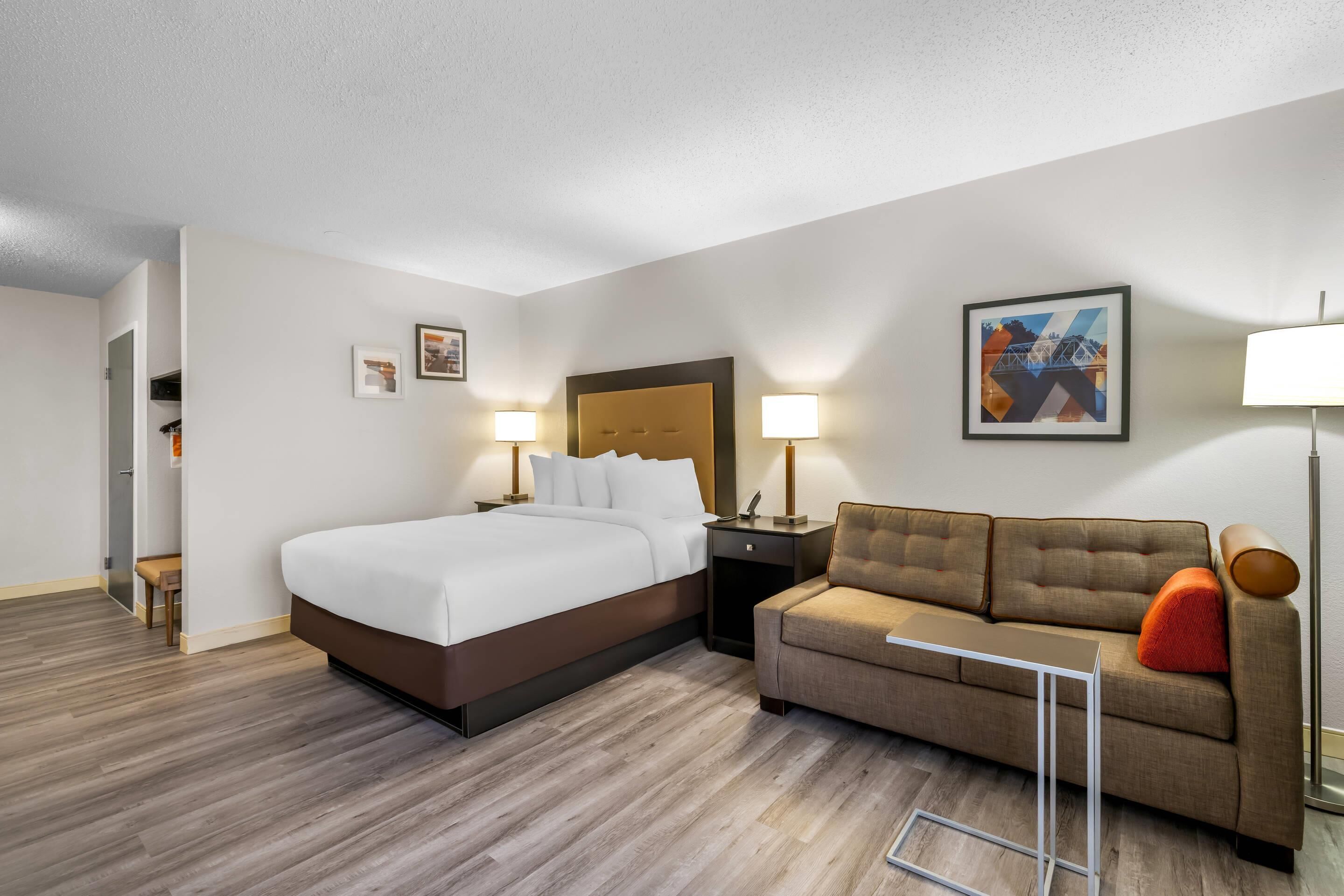 Una camera d'albergo con un letto, un divano, un comodino e una lampada fissata al muro.