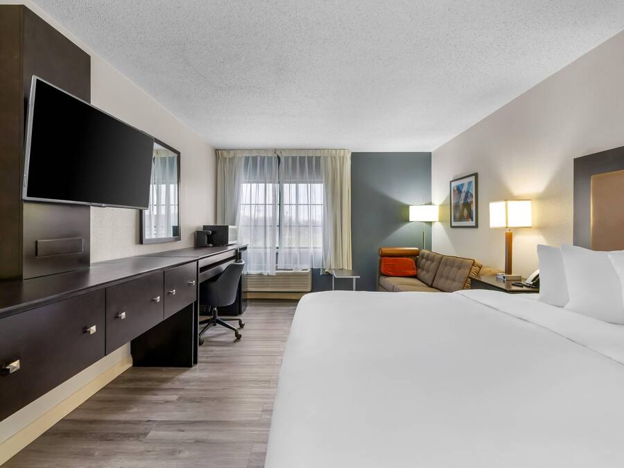 A hotel room with a bed, a desk with a chair, a television, a lamp, and a window with curtains.
