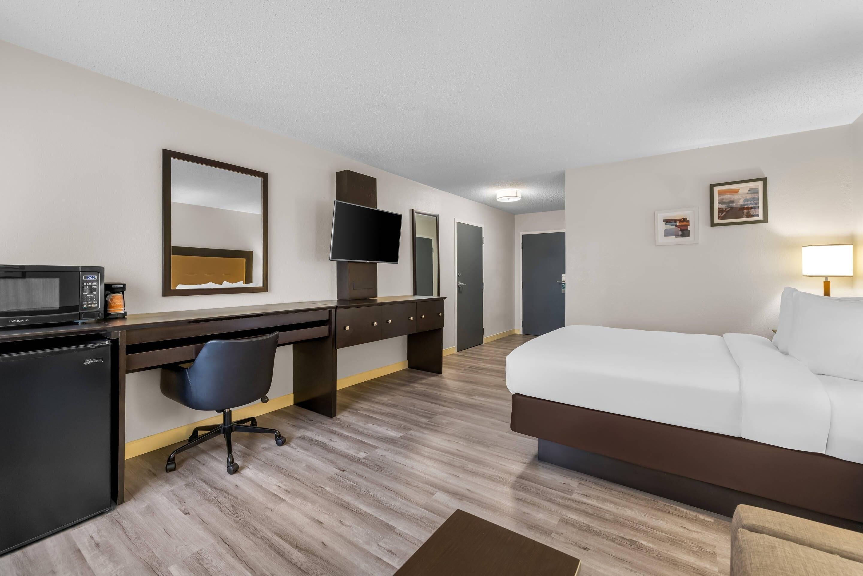Een hotelkamer met een bed, bureau, stoel, magnetron en televisie.