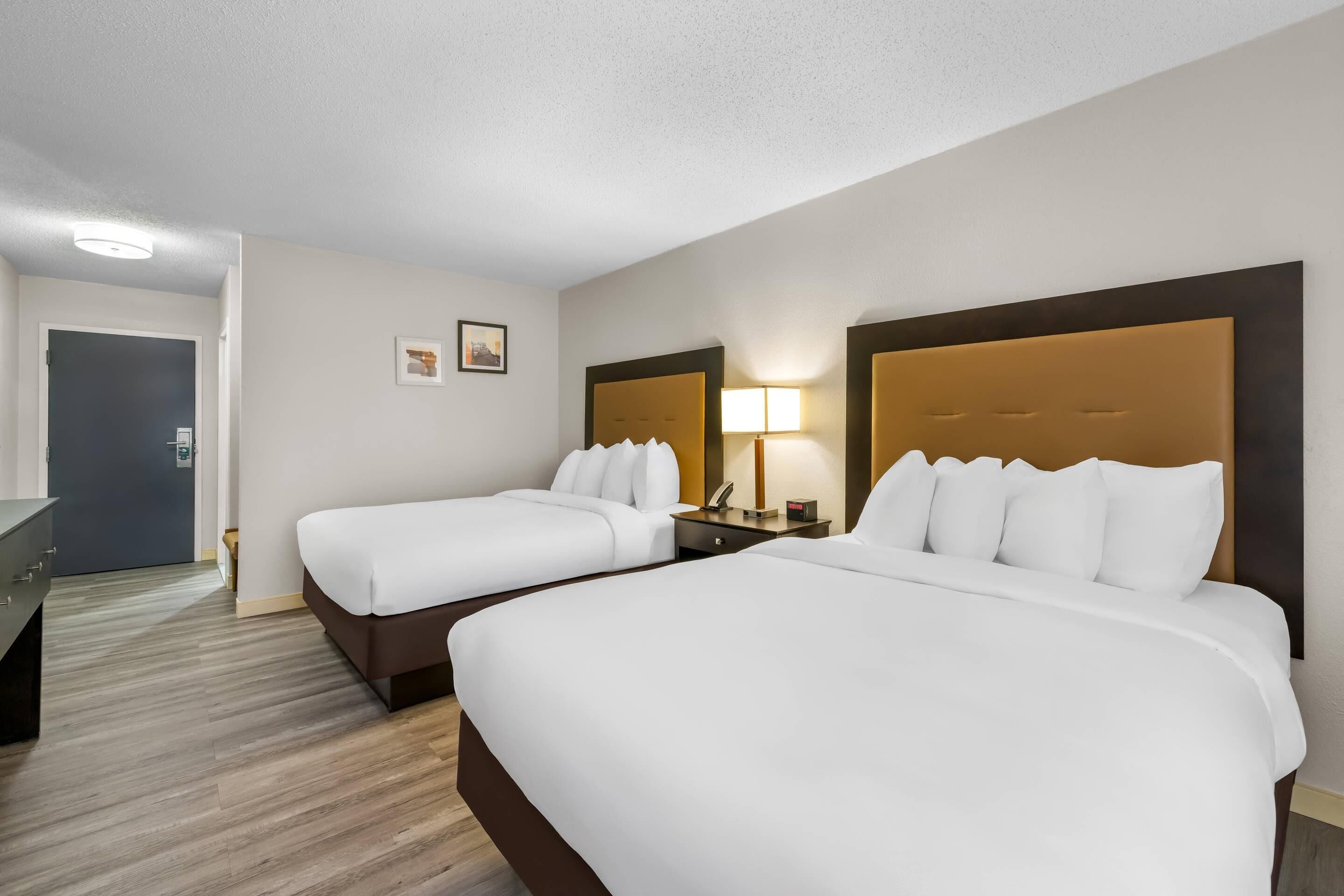 A hotel room with two beds, a desk, and a door.