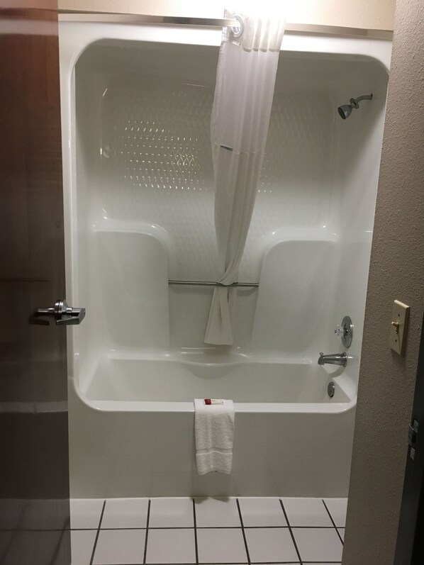 Una bañera blanca con cortina de ducha, una toalla colgada a un lado y un cabezal de ducha.