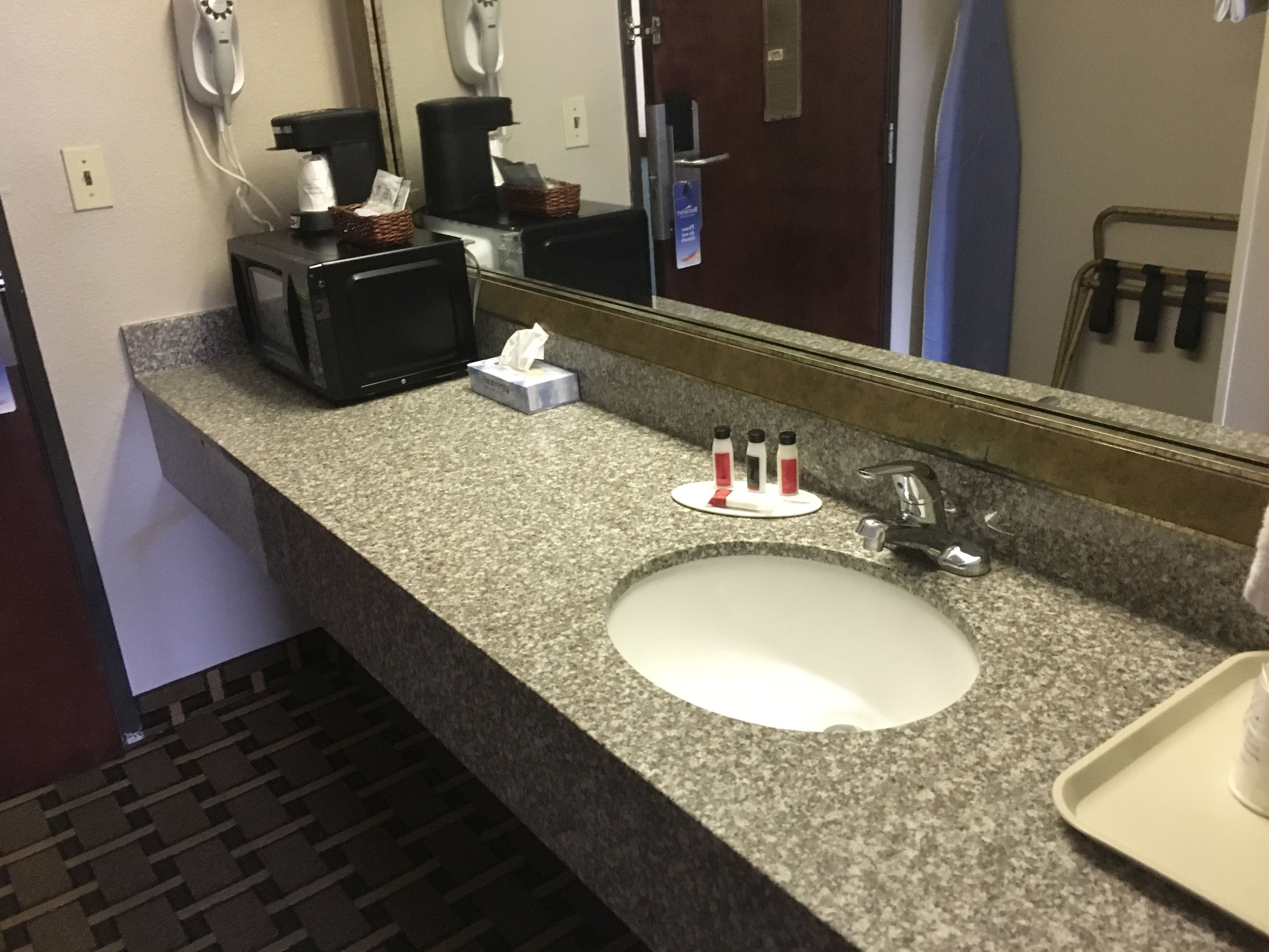 Une salle de bain d’hôtel avec un comptoir en granit, un lavabo, un miroir, une machine à café et des articles de toilette.