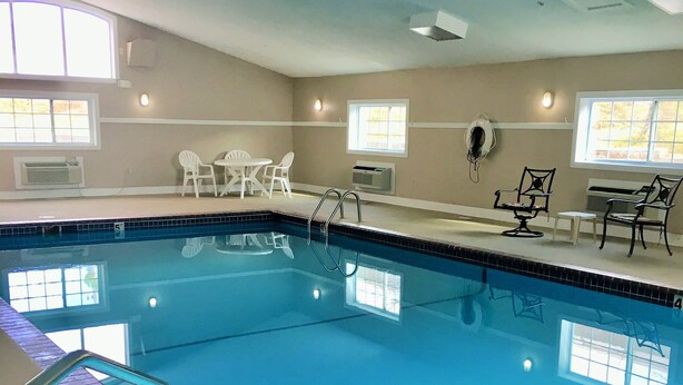 Une piscine intérieure à l’eau d’un bleu limpide, bordée de briques, et un espace aménagé au bord de la piscine avec des chaises et des tables.