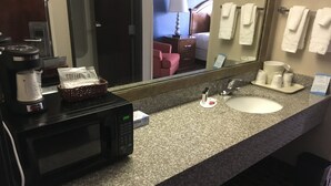 Une salle de bain d’hôtel équipée d’un plan de toilette en granit, d’un lavabo, d’un miroir, d’un four à micro-ondes et d’une machine à café.