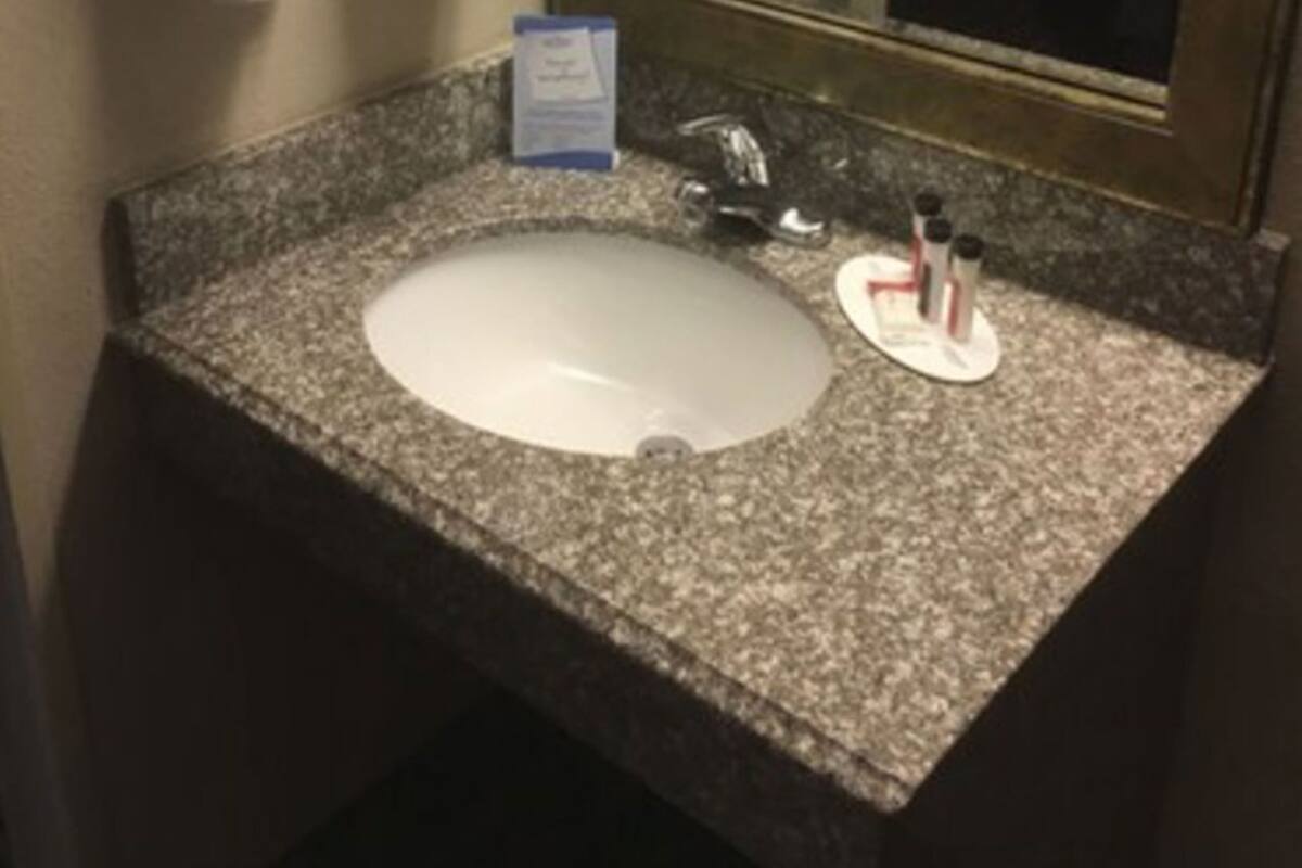 A bathroom with a granite countertop sink, a mirror, and towels hanging on a rack.