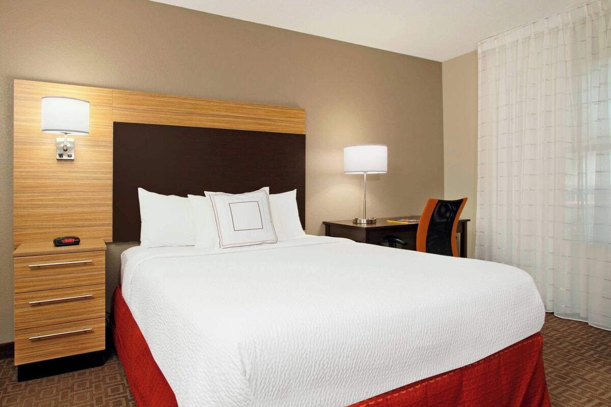 Une chambre d’hôtel avec un grand lit, un bureau, une chaise, une table de chevet et une lampe.