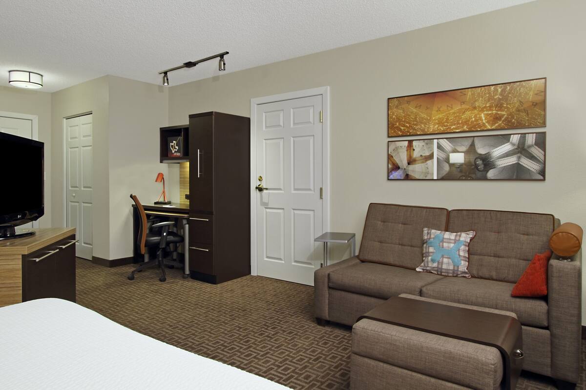 Une chambre d’hôtel comprenant un lit, un canapé, un bureau avec un ordinateur, une télévision et un mur décoré d’œuvres d’art.