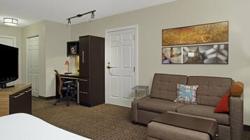 A hotel room with a bed, a sofa, a desk with a computer, a TV, and a wall with artwork.