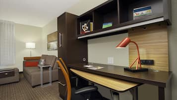 Quarto de hotel com escrivaninha, cadeira, sofá e luminária.