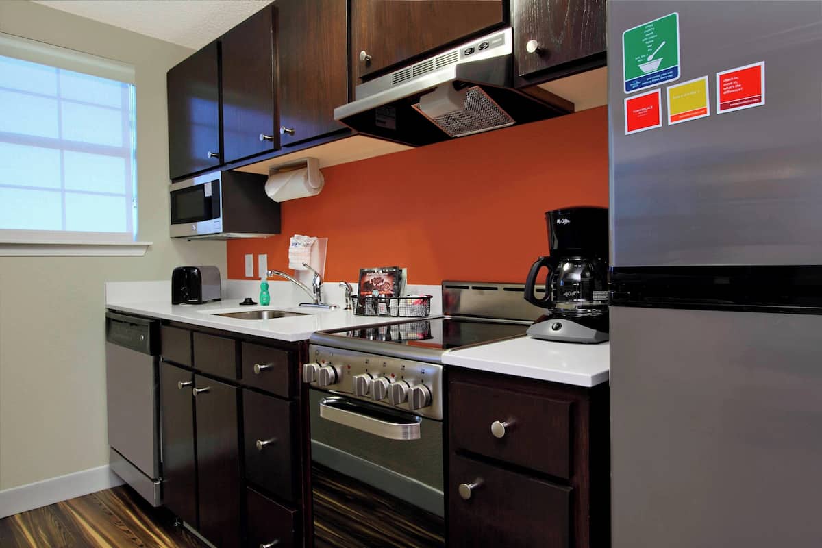 Une cuisine moderne avec des meubles de couleur sombre, des appareils en acier inoxydable et un mur d’accent rouge.