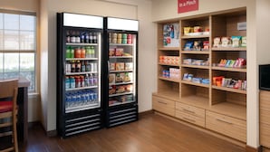 Ein Hotelzimmer mit Minibar, einer Sitzecke mit Tisch und Stühlen sowie einem mit Snacks und Getränken gefüllten Regal.