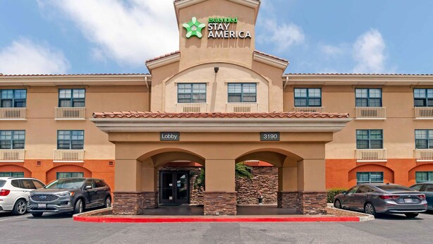 A hotel with a sign reading 'Extended Stay America,' featuring a lobby entrance, multiple balconies, and a parking lot with several cars. - Extended Stay America Suites San Diego Oceanside (Oceanside)